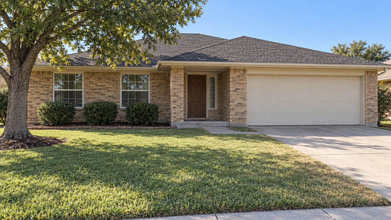 A buff-brick ranch with a broad front lawn, mature oak, recessed porch and attached garage in clear autumn daylight.