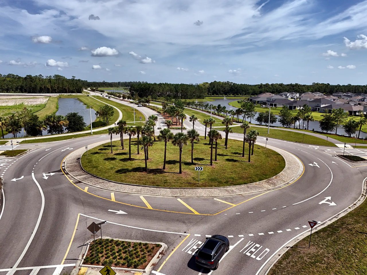 Aerial view of a palm-lined roundabout, with neighborhood homes and ponds nearby.