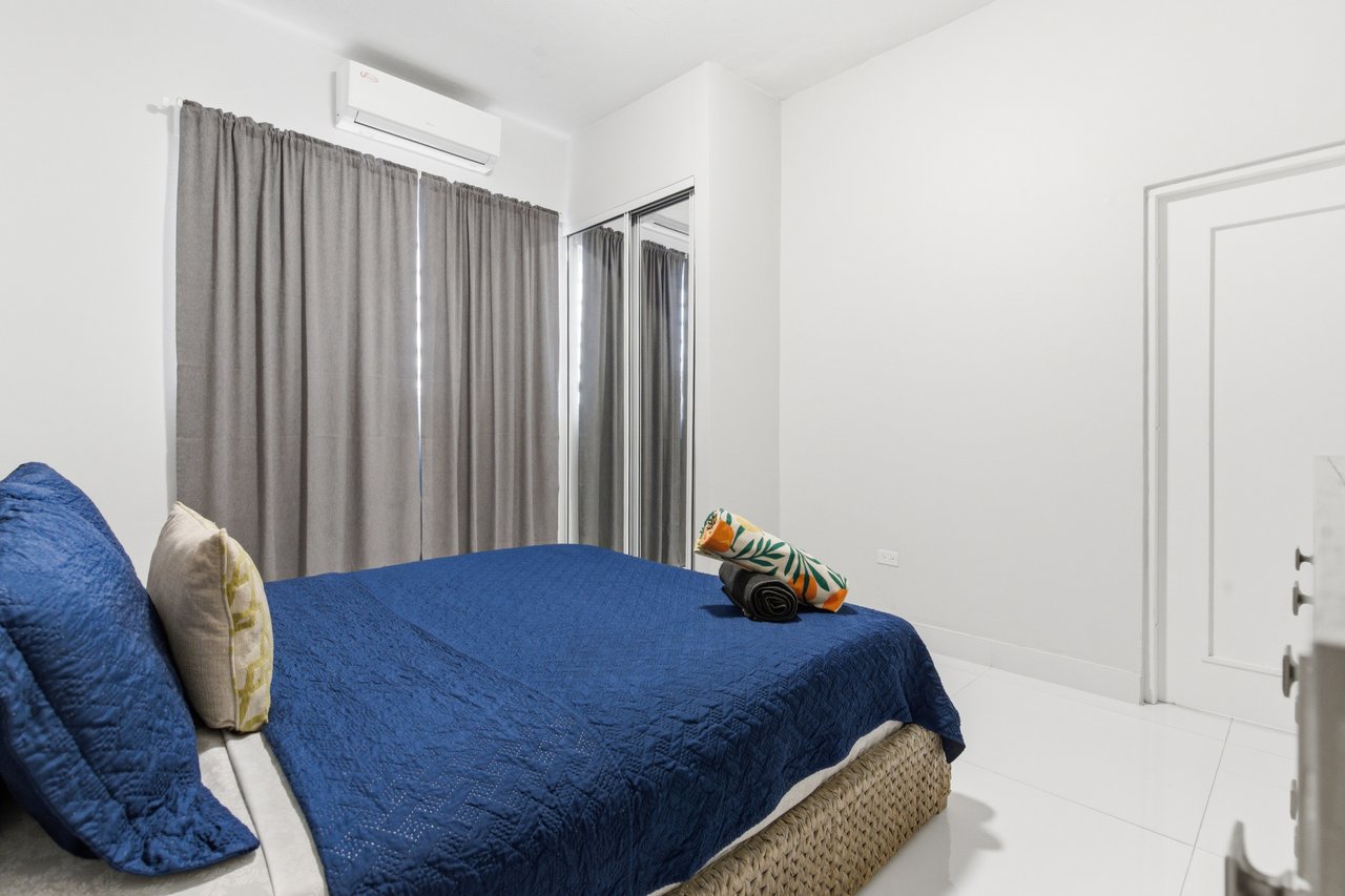 Bedroom with a dark blue quilted bed, gray curtains, and a wall-mounted air conditioner.