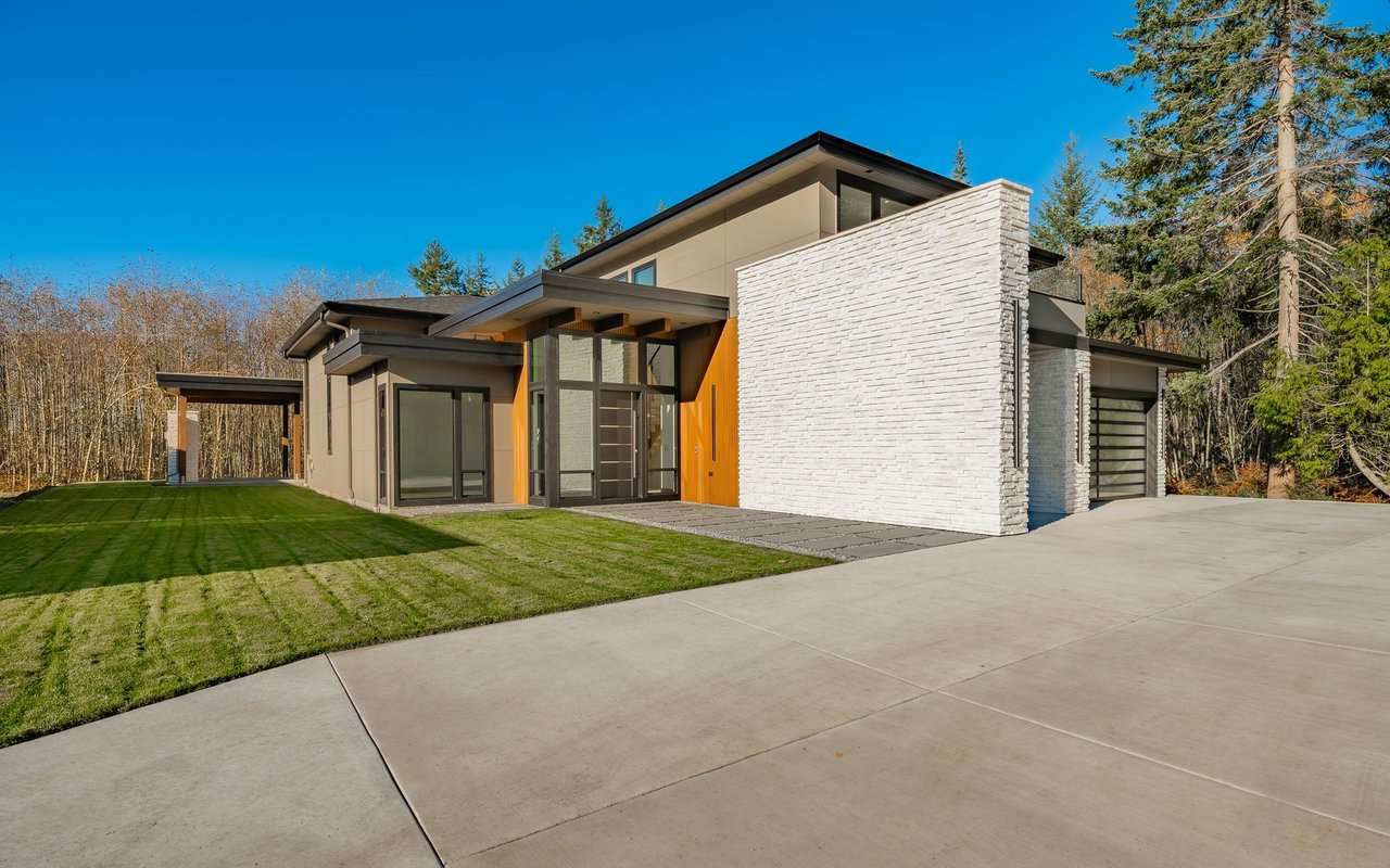 Modern home with a white stone facade, orange entry accent, broad driveway, and striped lawn.