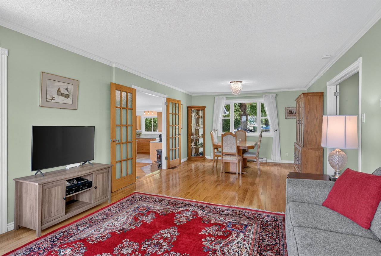 Living and dining room with hardwood floors, a red patterned rug, and open French doors to the kitchen.