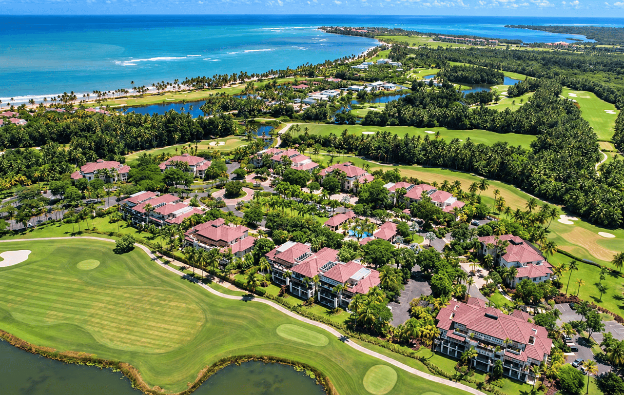 Coastal condominium community beside a golf course, with palm trees, lagoons, and blue ocean.