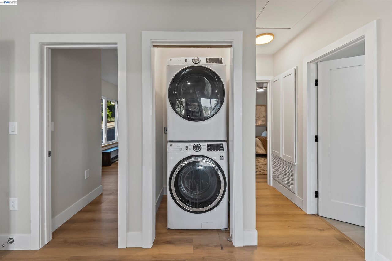 Laundry area with a stacked white washer and dryer between two open hallways.