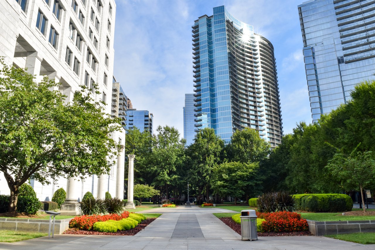 Modern condominium towers overlook a landscaped plaza with trees and flower beds.