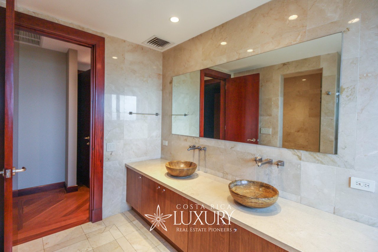 Marble bathroom with double vessel sinks, a wood vanity, and a large wall mirror.