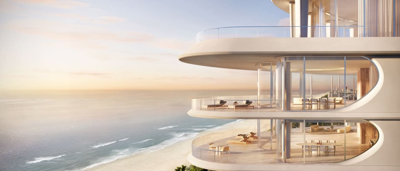 Curved oceanfront residences with glass balconies overlook a beach at golden hour.