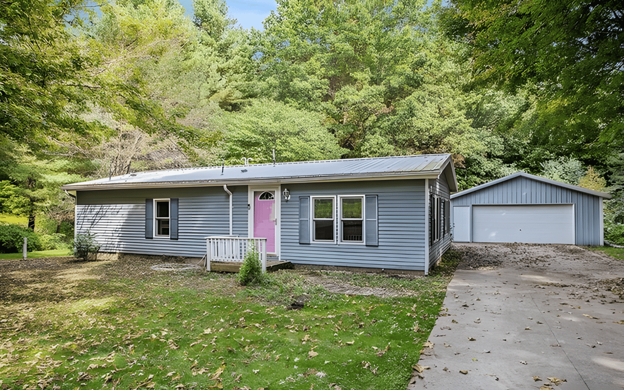 Gray single-story home with a pink front door and detached garage amid mature trees.