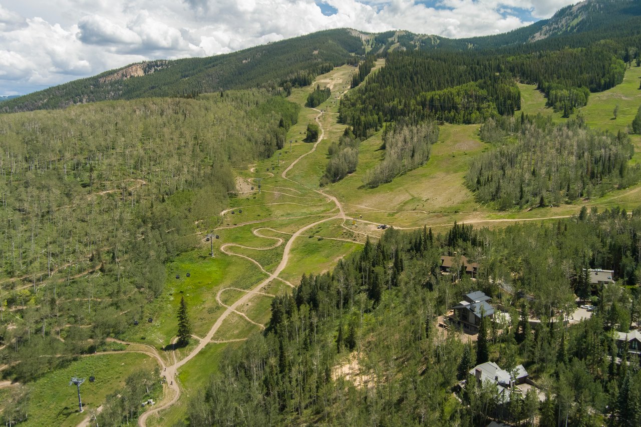 Aerial view of ski trails winding through forested mountain slopes above nearby homes.