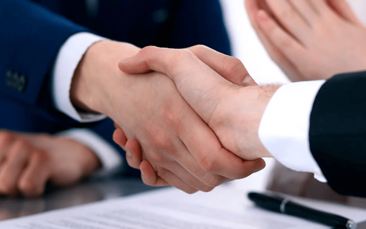 Businesspeople shake hands over paperwork beside a pen.
