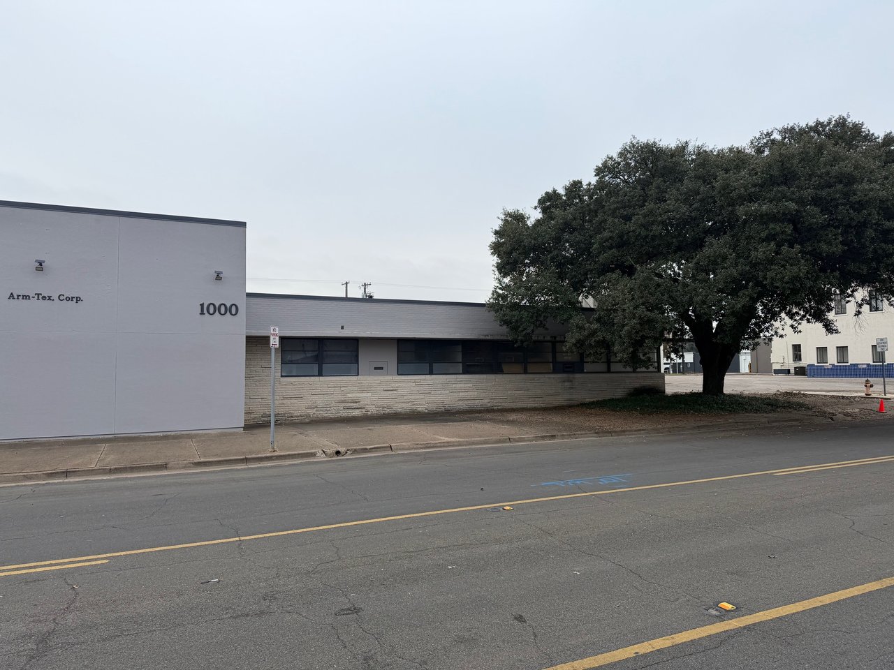 Low-rise commercial building marked Arm-Tex Corp. and 1000, with a large tree beside the sidewalk.