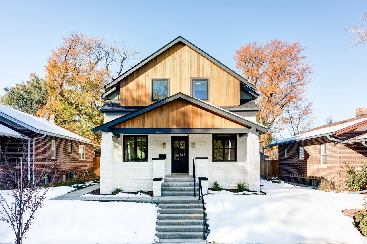 Two-story modern craftsman home with white brick base, natural wood siding, and black-trimmed windows in snow-covered setting