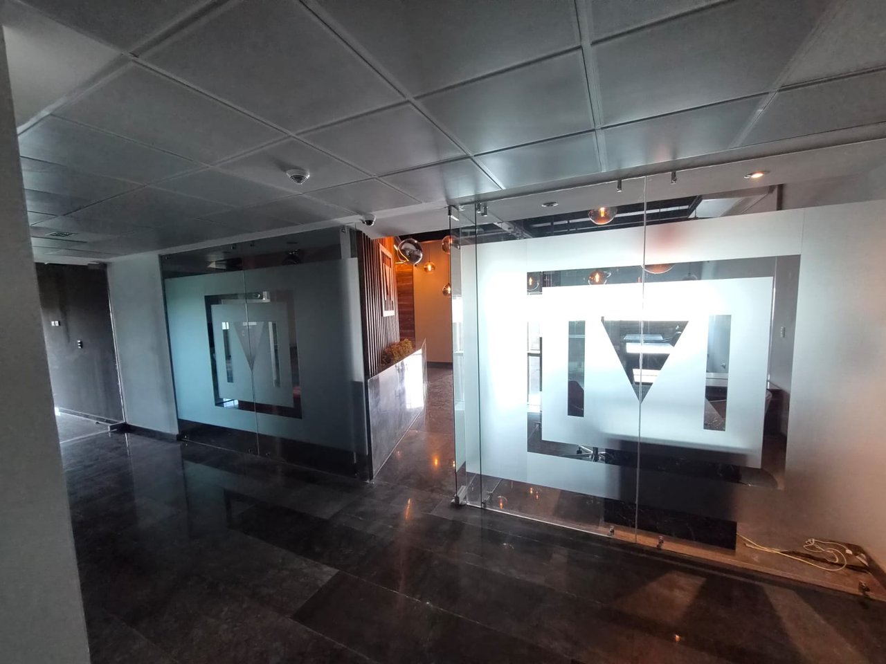 Office reception area with glass partitions, frosted graphics, and dark tiled floors.