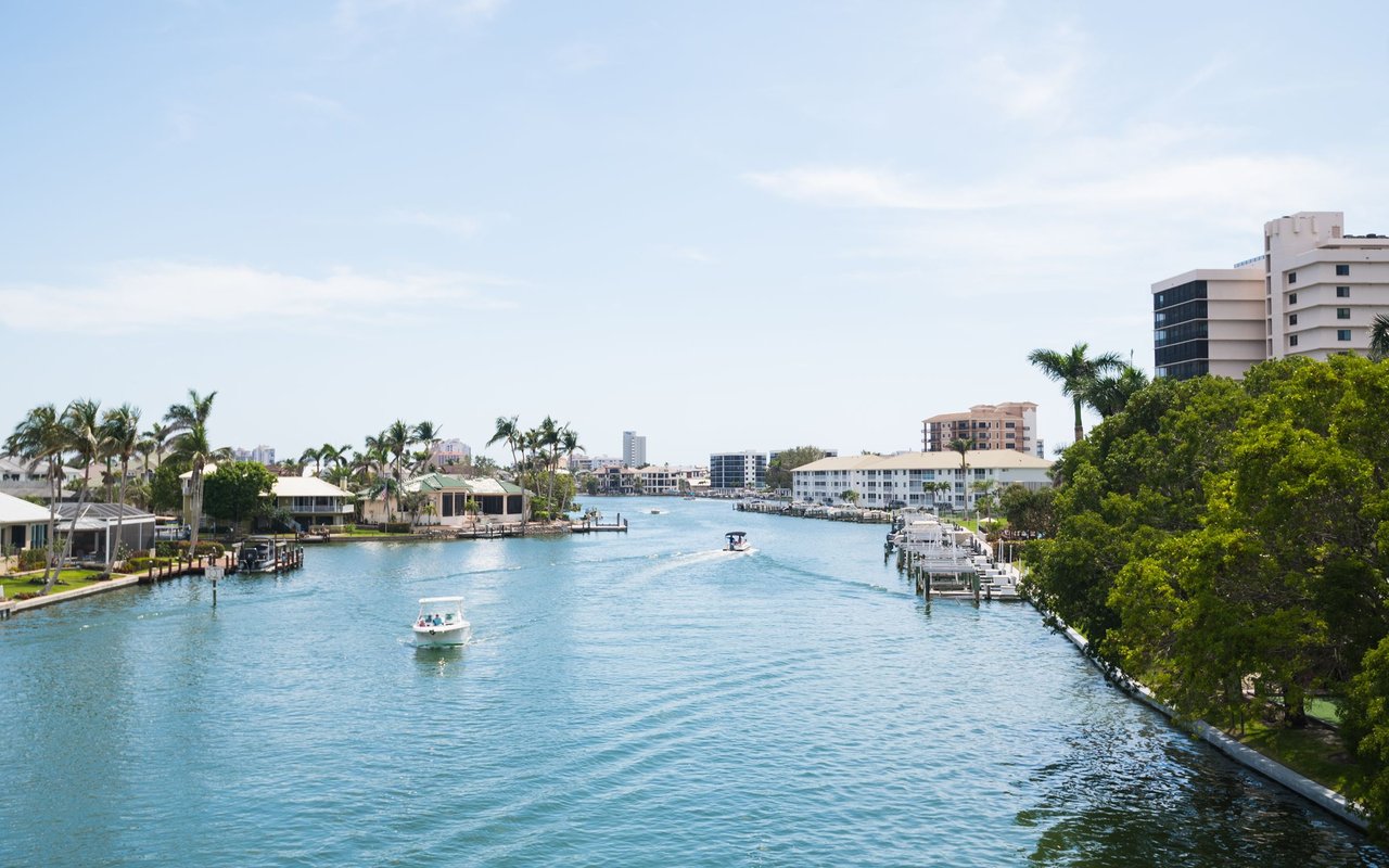 Waterfront canal with homes, docks, palm trees, and two boats on the water.