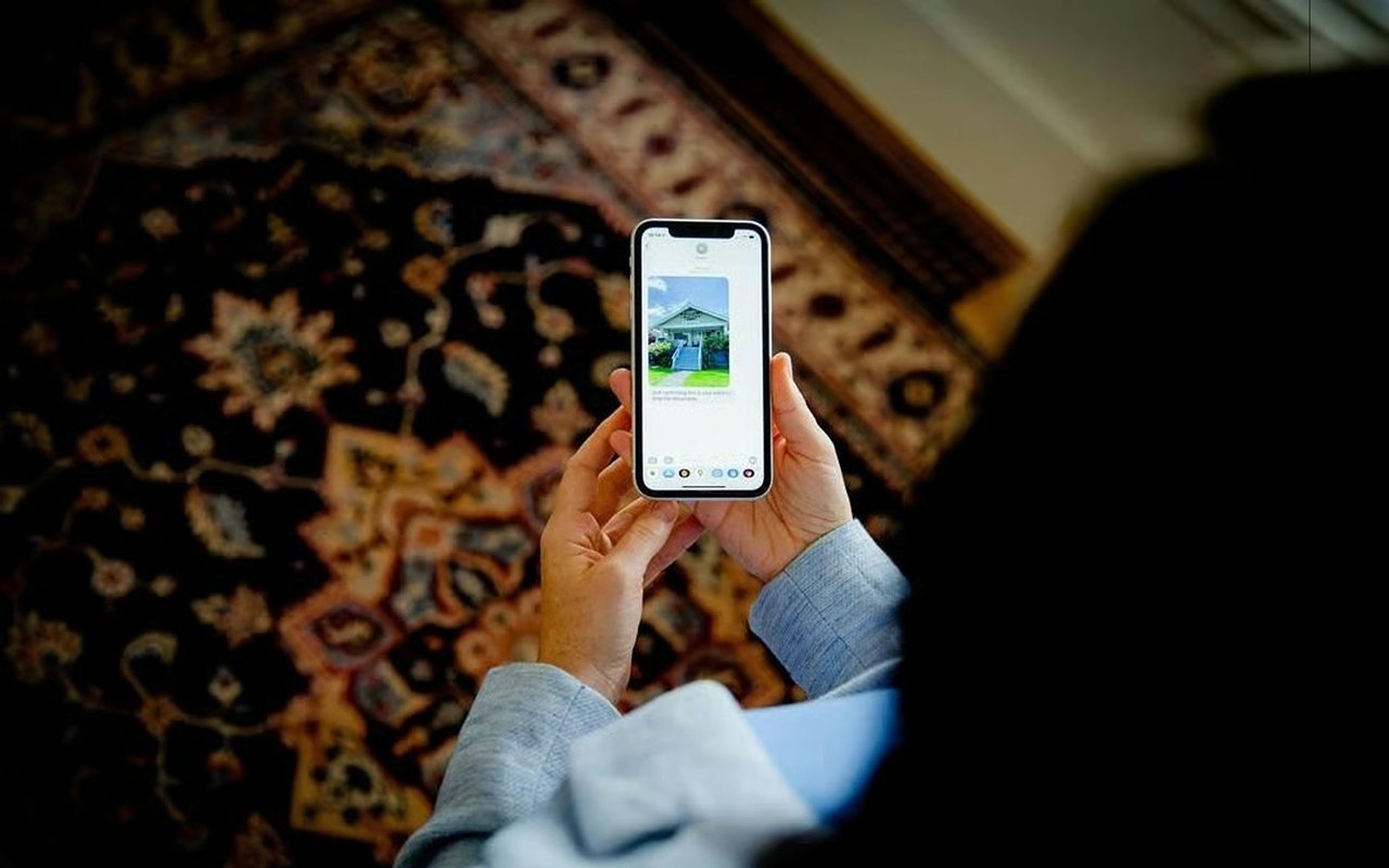 Hands holding a phone display a house listing over a patterned rug.