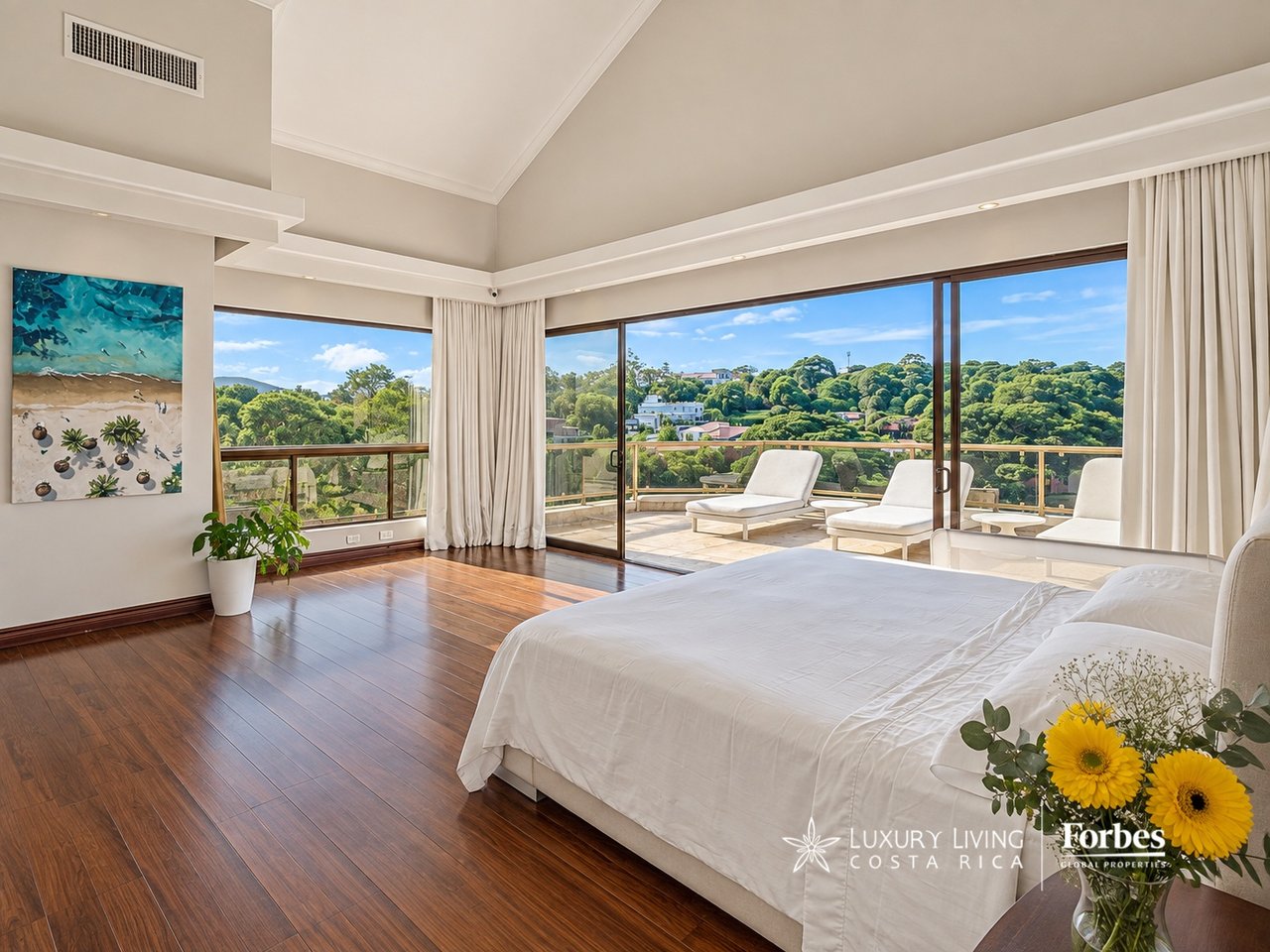 Penthouse bedroom opening onto a private terrace with loungers and a view of tree-covered hills.