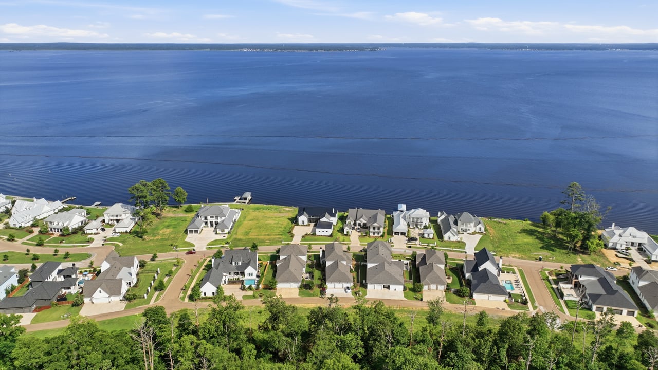 Aerial view of lakeside homes bordering expansive blue water and a green shoreline.
