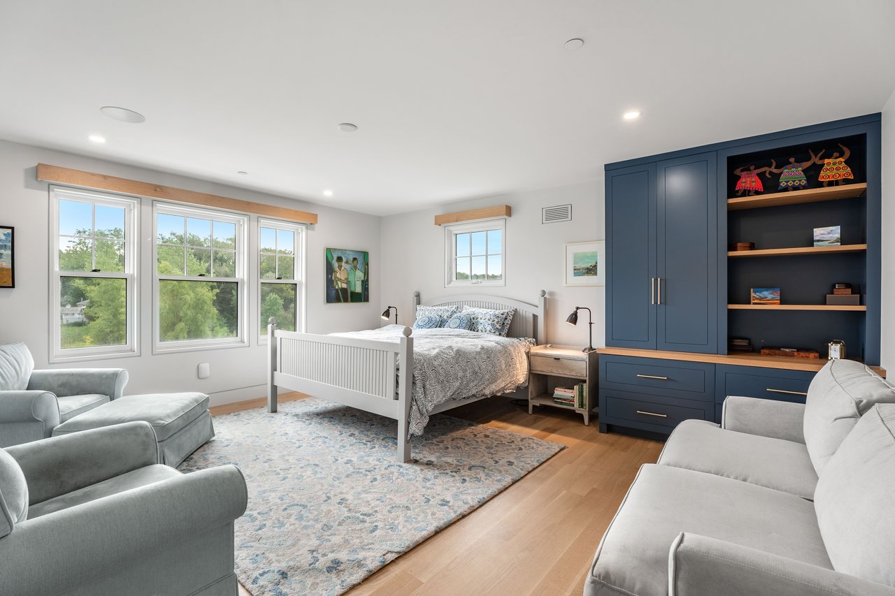 Bedroom with a white bed, navy-blue built-in cabinetry, and a seating area beside large windows.