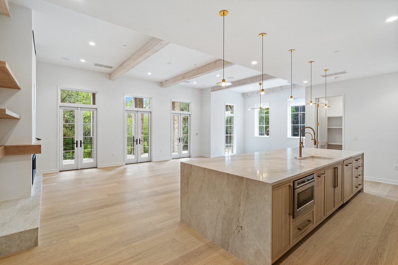 Vacant luxury kitchen with a marble waterfall island and tall French doors opening to greenery.