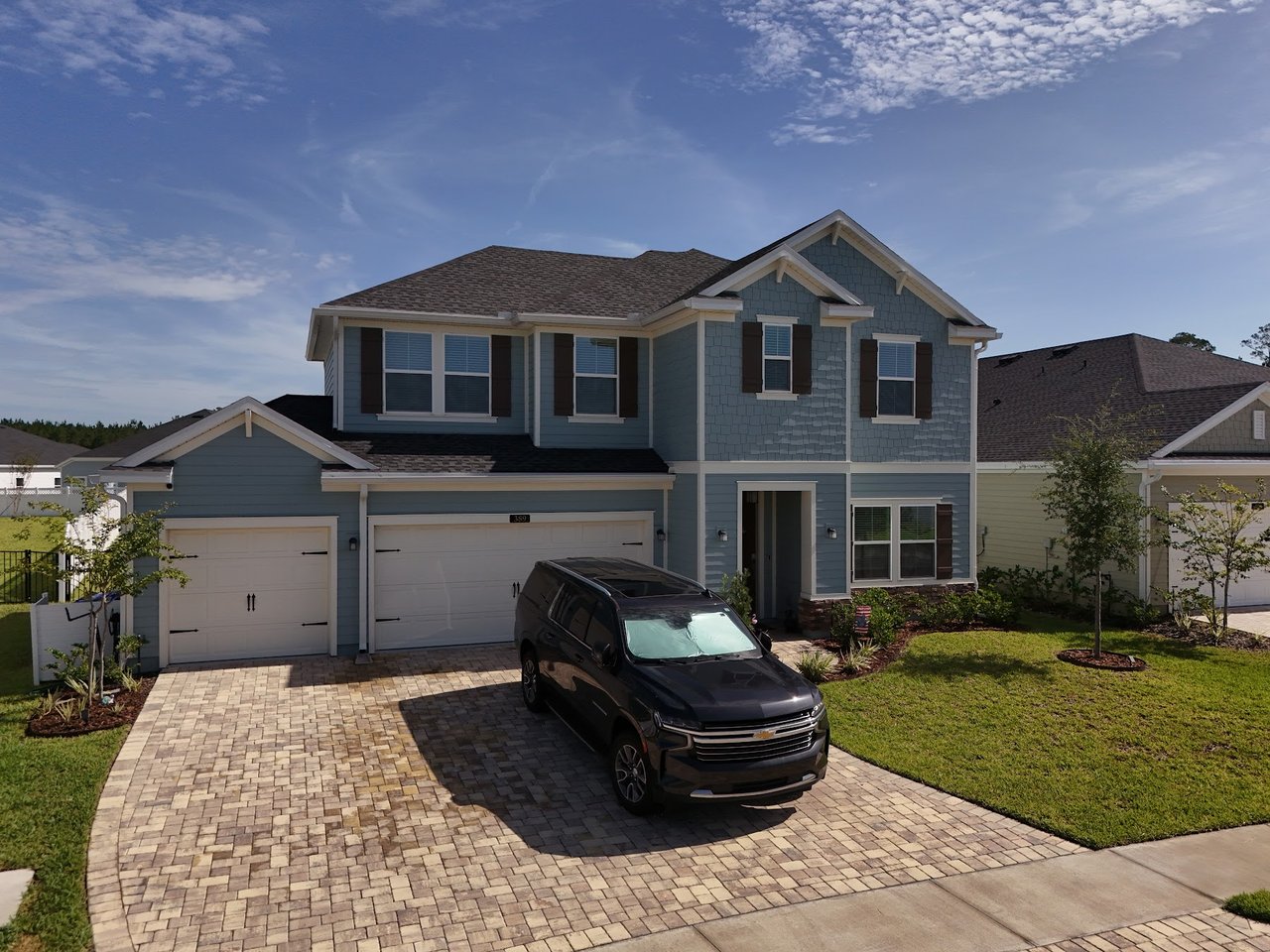 Two-story blue-gray house with white trim, a multi-car garage, and a dark SUV in the driveway.
