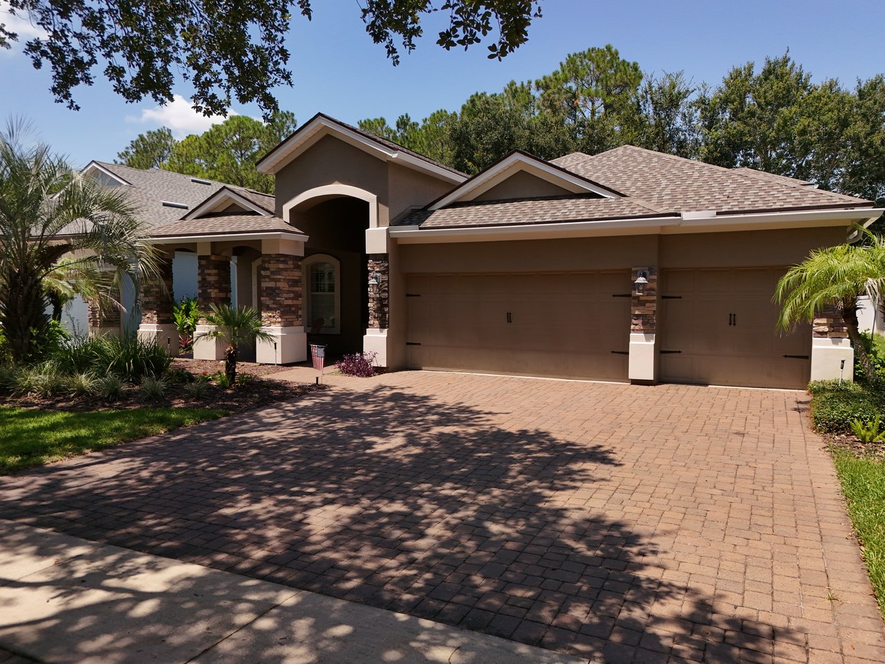 Single-story home with a three-car garage, stone-accented entry, and wide paver driveway.