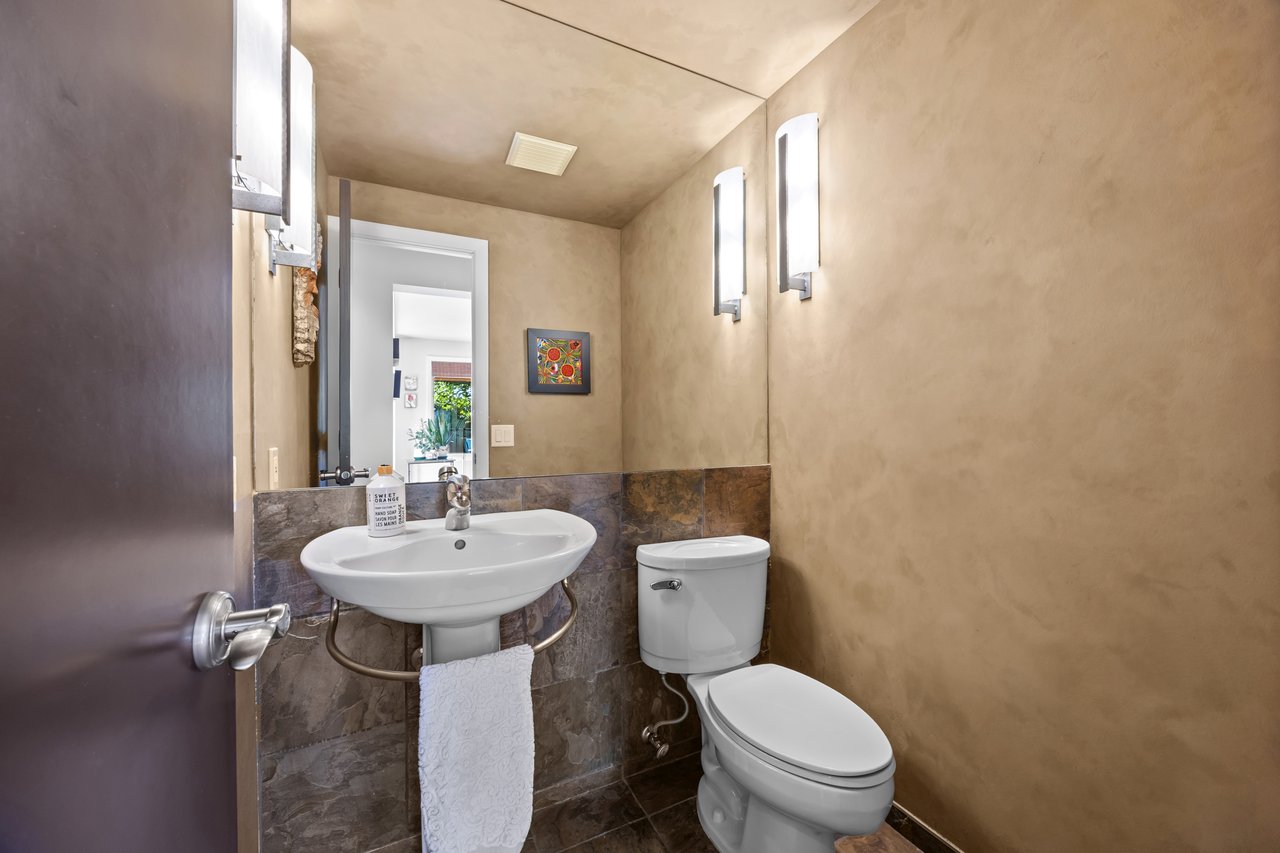 Bathroom with a pedestal sink, toilet, dark stone tile, and modern wall sconces.
