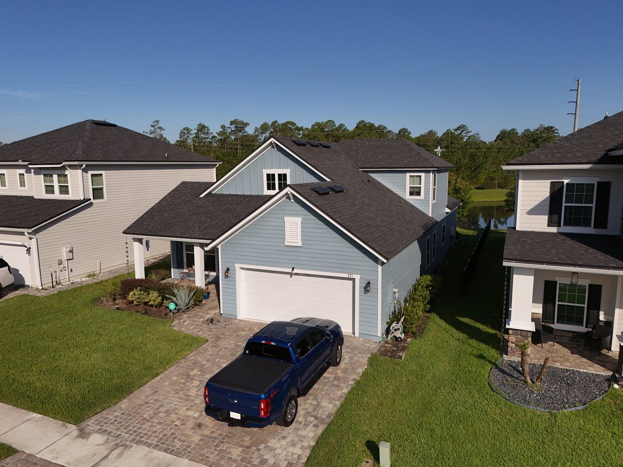 Blue-gray home with a white double garage, brick-paver driveway, and pond behind it.