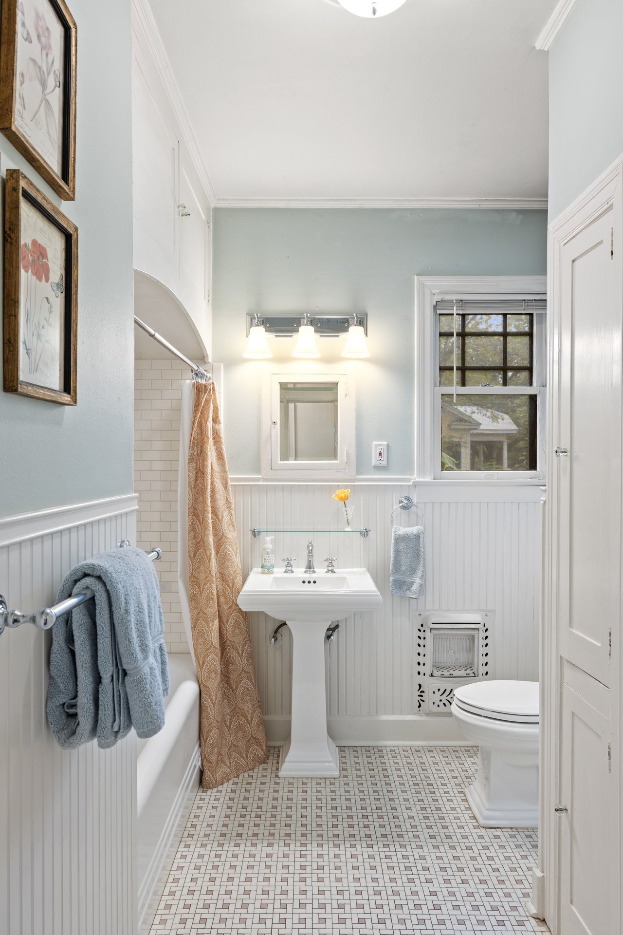Bathroom with a pedestal sink, mosaic tile floor, beadboard walls, and a window above the toilet.