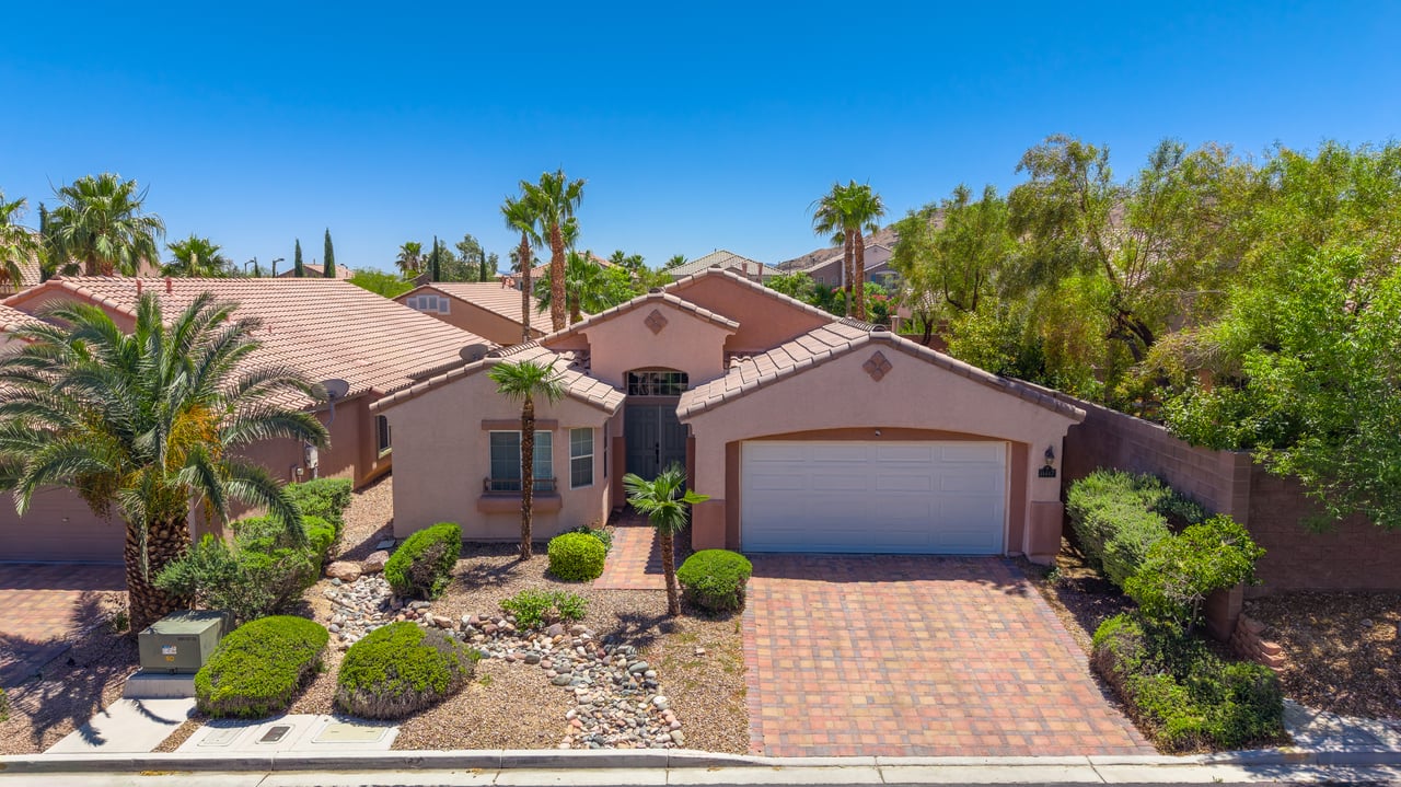 Single-story stucco home with a tiled roof, palm trees, and a broad paver driveway.
