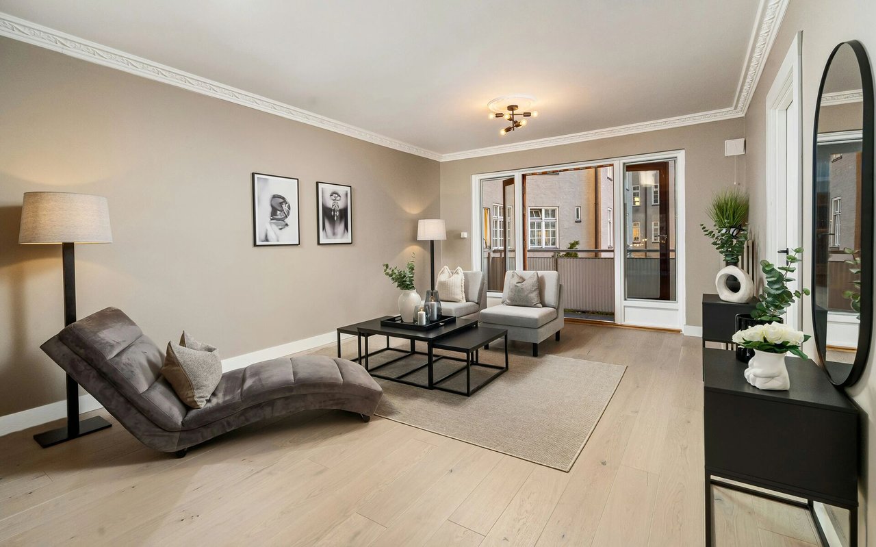 Staged living room with a gray chaise lounge, neutral furnishings, and glass doors opening to a balcony.