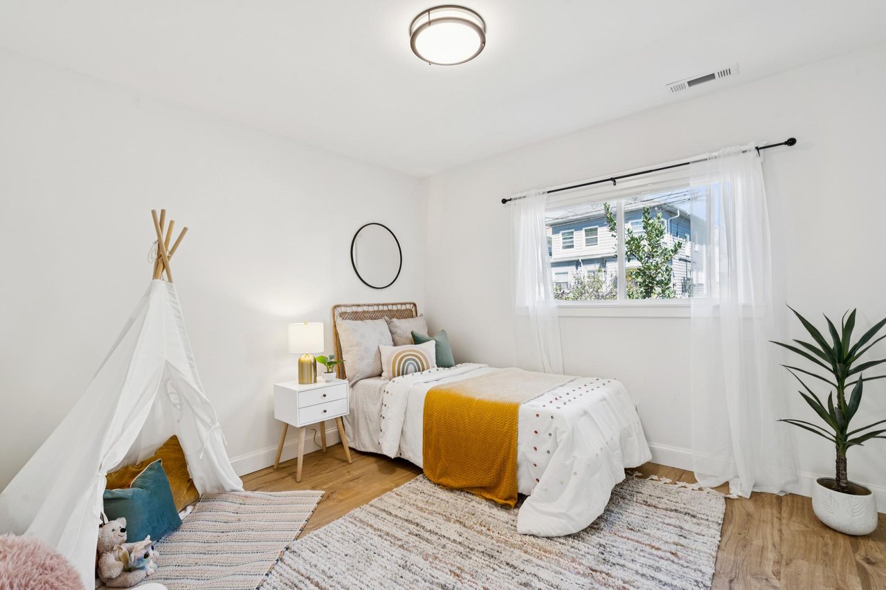 Bright bedroom with a white-and-mustard bed, teepee play tent, and window with sheer curtains.