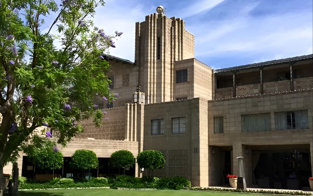 Geometric stone building with a tall central tower and flowering trees in the foreground.