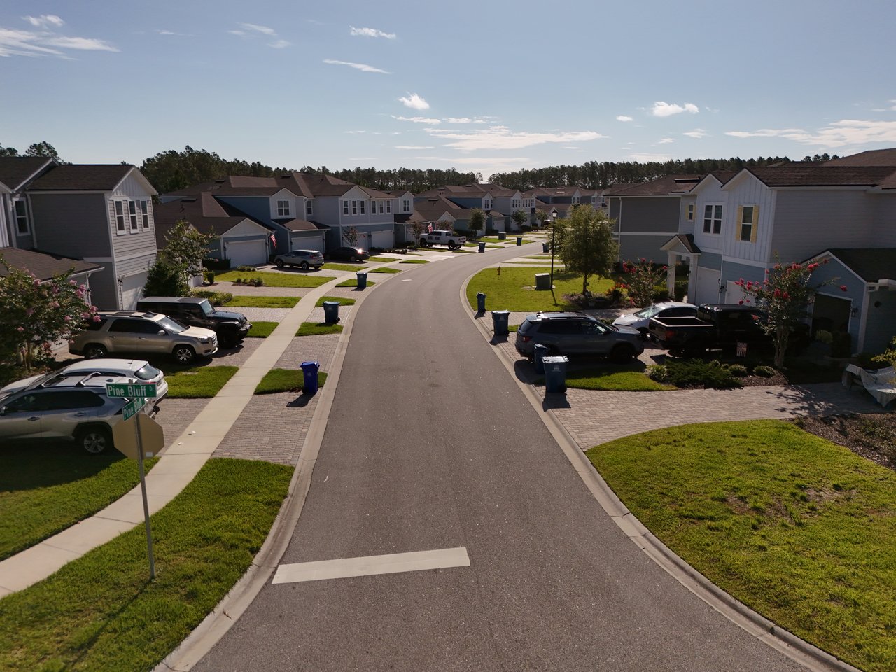 Curving residential street lined with two-story homes, sidewalks, lawns, and parked cars.
