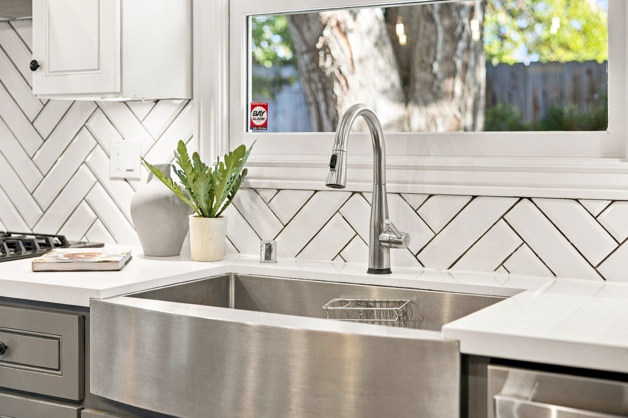 Kitchen sink with a stainless steel apron front, gooseneck faucet, and white herringbone tile backsplash.
