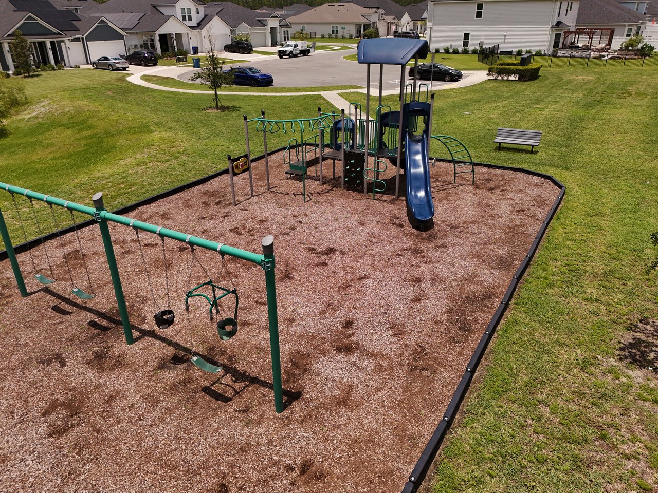 Neighborhood playground with a blue slide and swings beside residential homes.