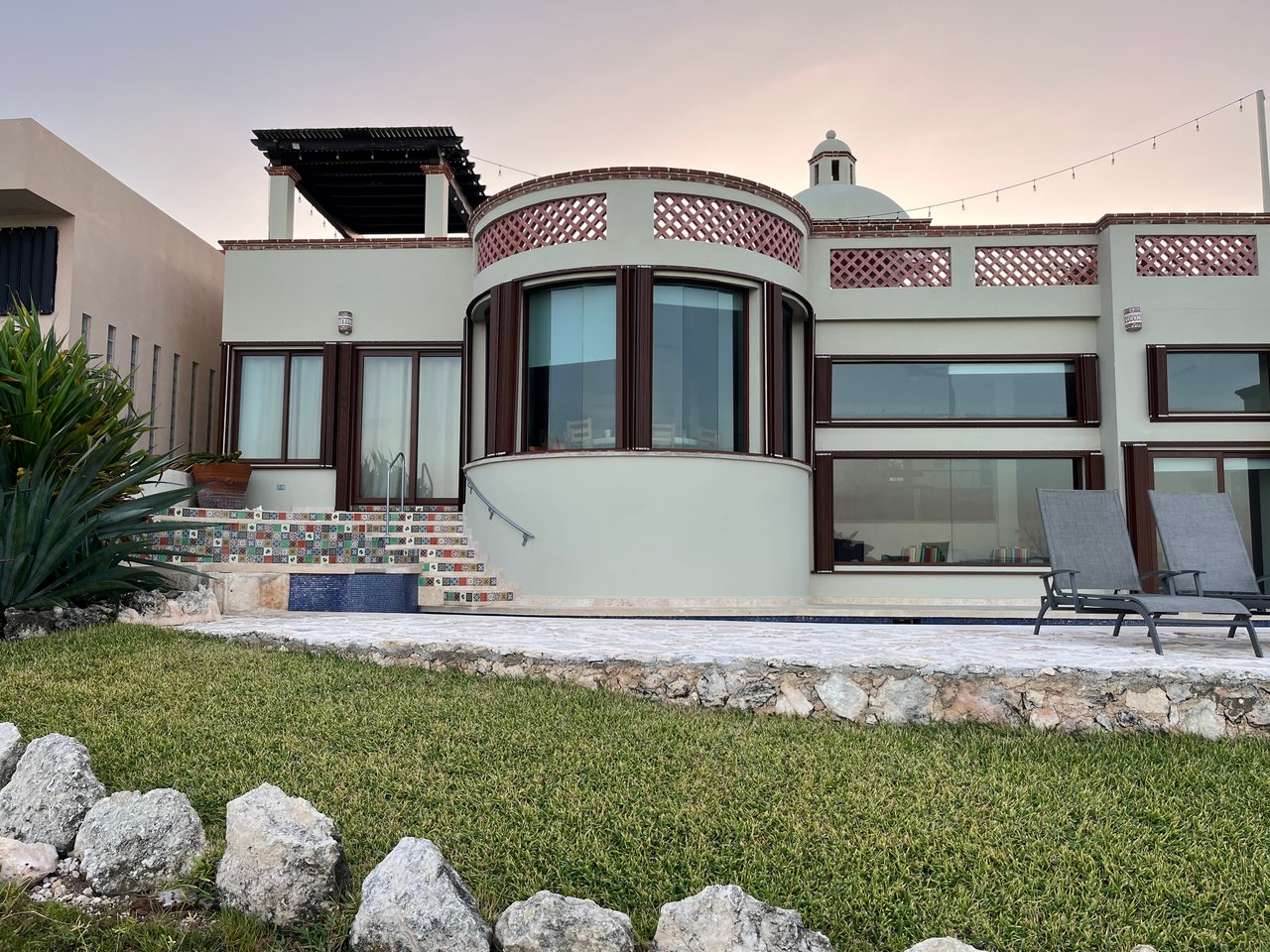 Modern white house with a curved glass facade, tiled pool, and lawn.