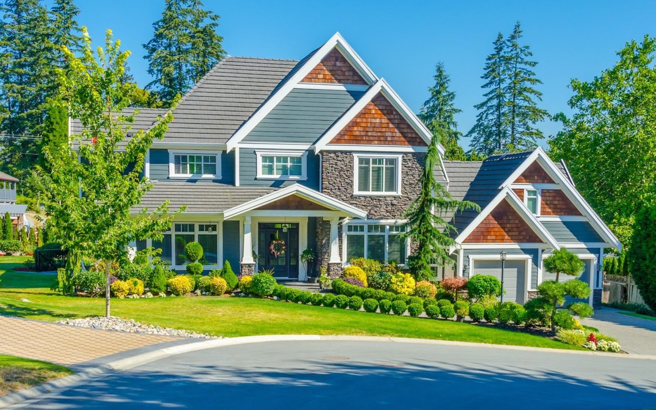 Luxury craftsman estate showcasing blue lap siding, natural stone accents, cedar shake gables, a columned portico entryway, and professional topiary landscaping on a cul-de-sac.
