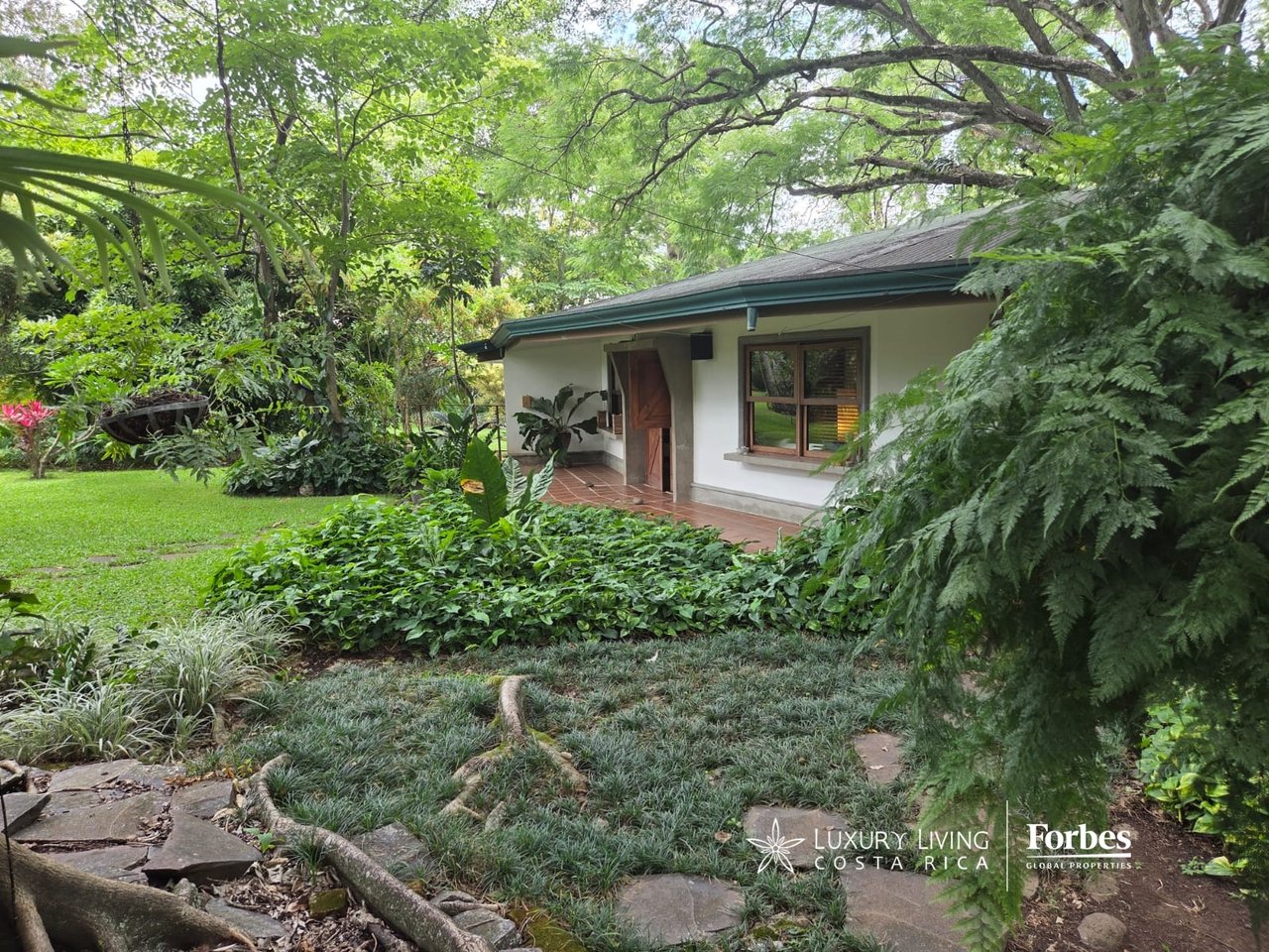Single-level villa nestled in a lush tropical garden, with a tiled porch and stone paths.