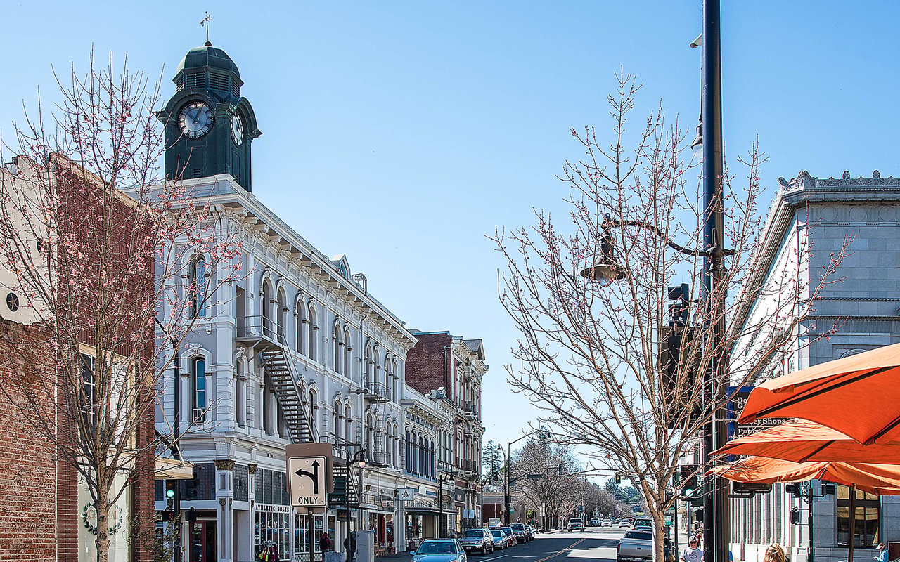 Downtown Petaluma street with a prominent clock tower, historic buildings, and orange café awnings.