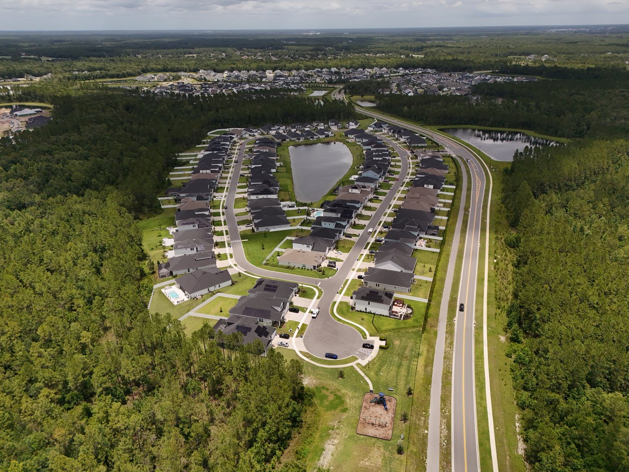 Aerial view of a wooded residential community with homes arranged around a pond and curving streets.