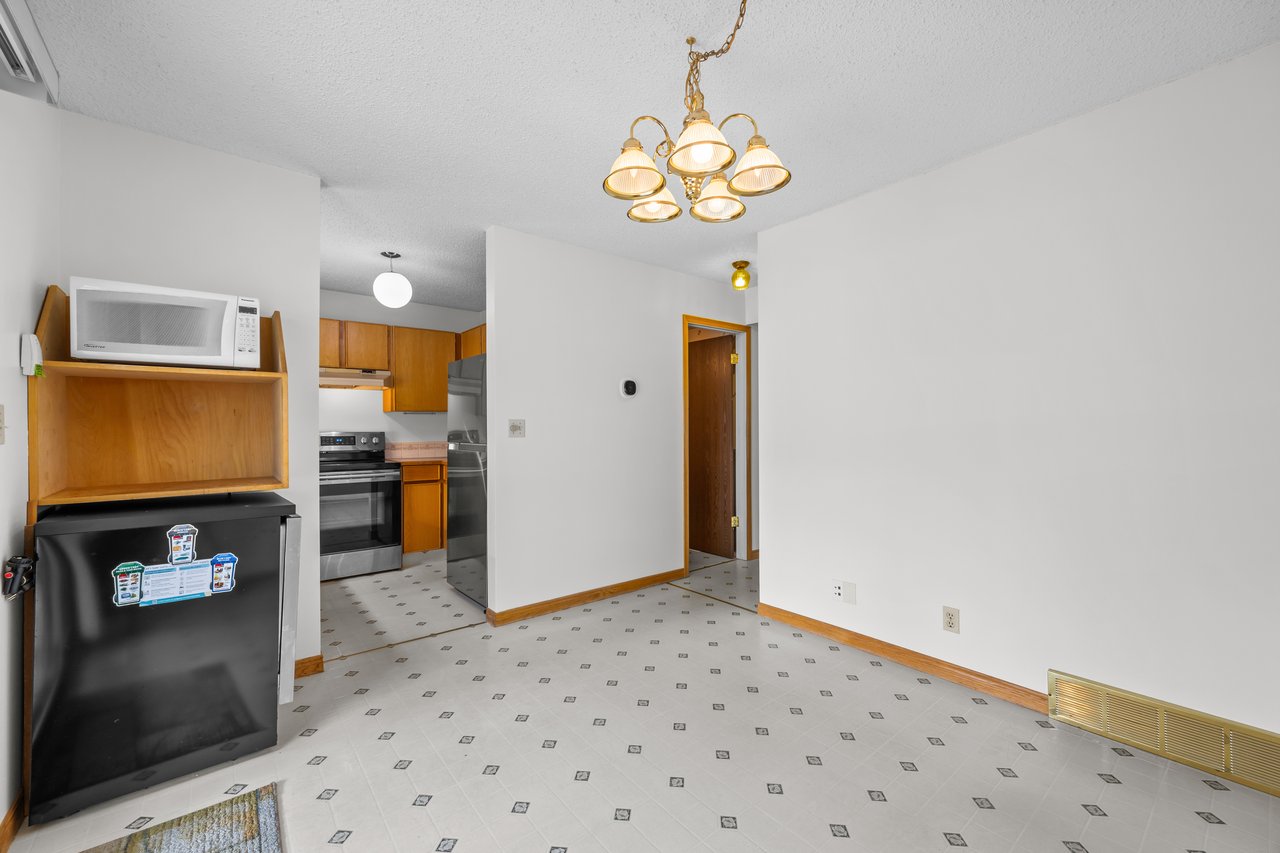 Unfurnished dining area with patterned tile flooring, brass chandelier, and adjoining wood-cabinet kitchen.