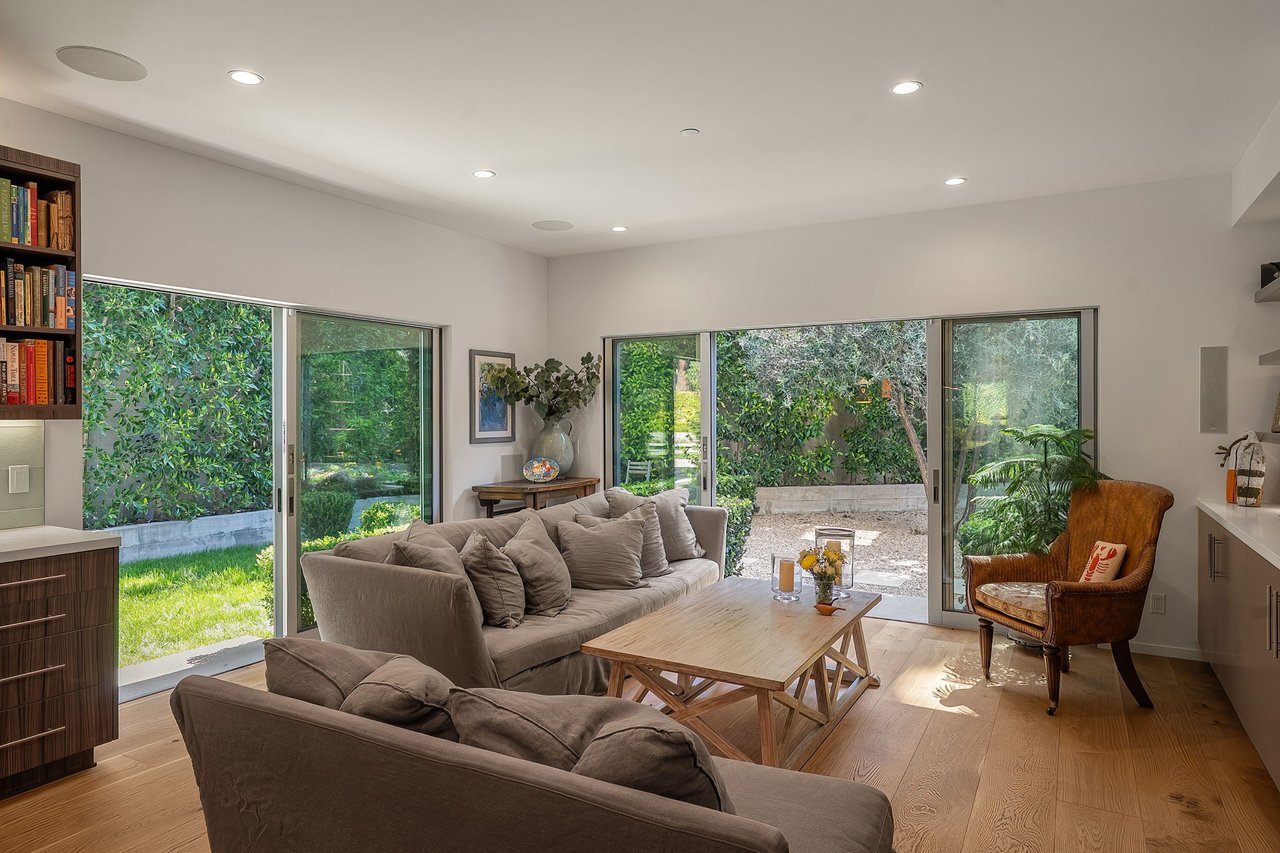 Living room with taupe sofas and a leather armchair facing sliding doors to a leafy garden.