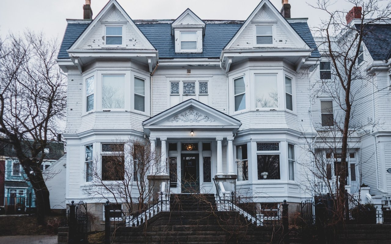 White historic Victorian house with ornate trim, twin bay windows, and a columned front porch.
