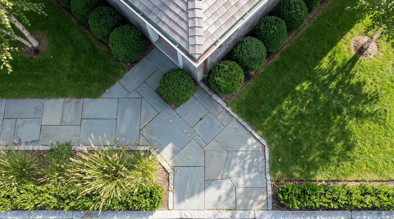 Overhead view of a diagonal bluestone walkway bordered by clipped boxwood, lawn, and ornamental grasses.