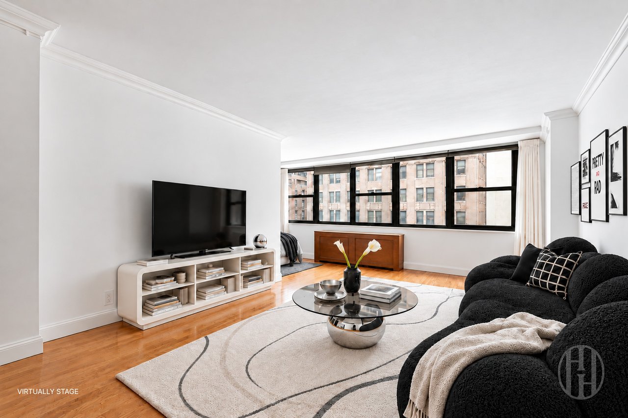 Virtually staged living room with black sofas, a glass coffee table, and broad windows facing nearby buildings.