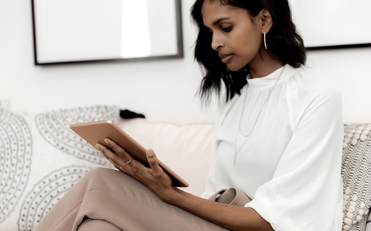 Woman in a white blouse using a tablet while seated on a patterned sofa.