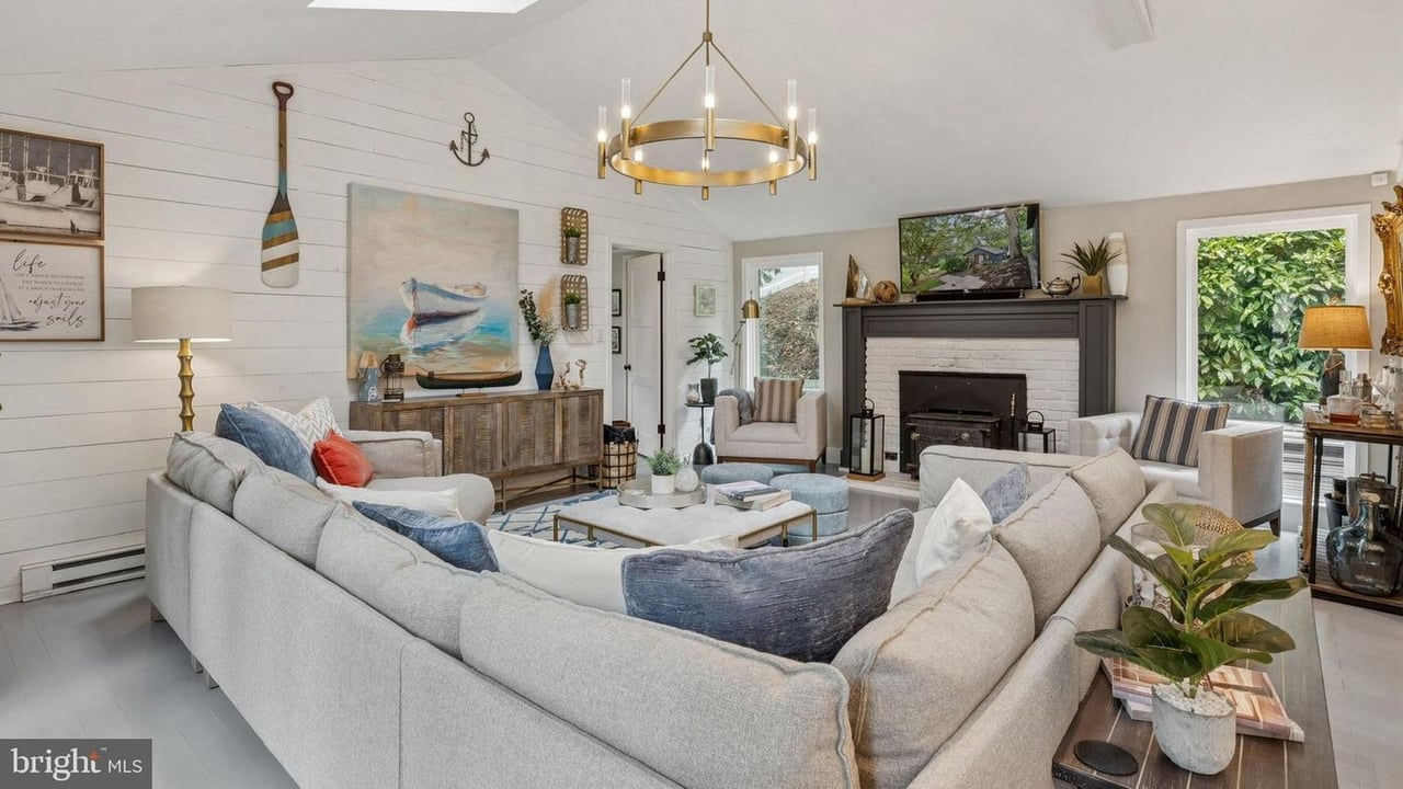 Furnished living room with a dark fireplace, brass chandelier, and pale sectional sofas.