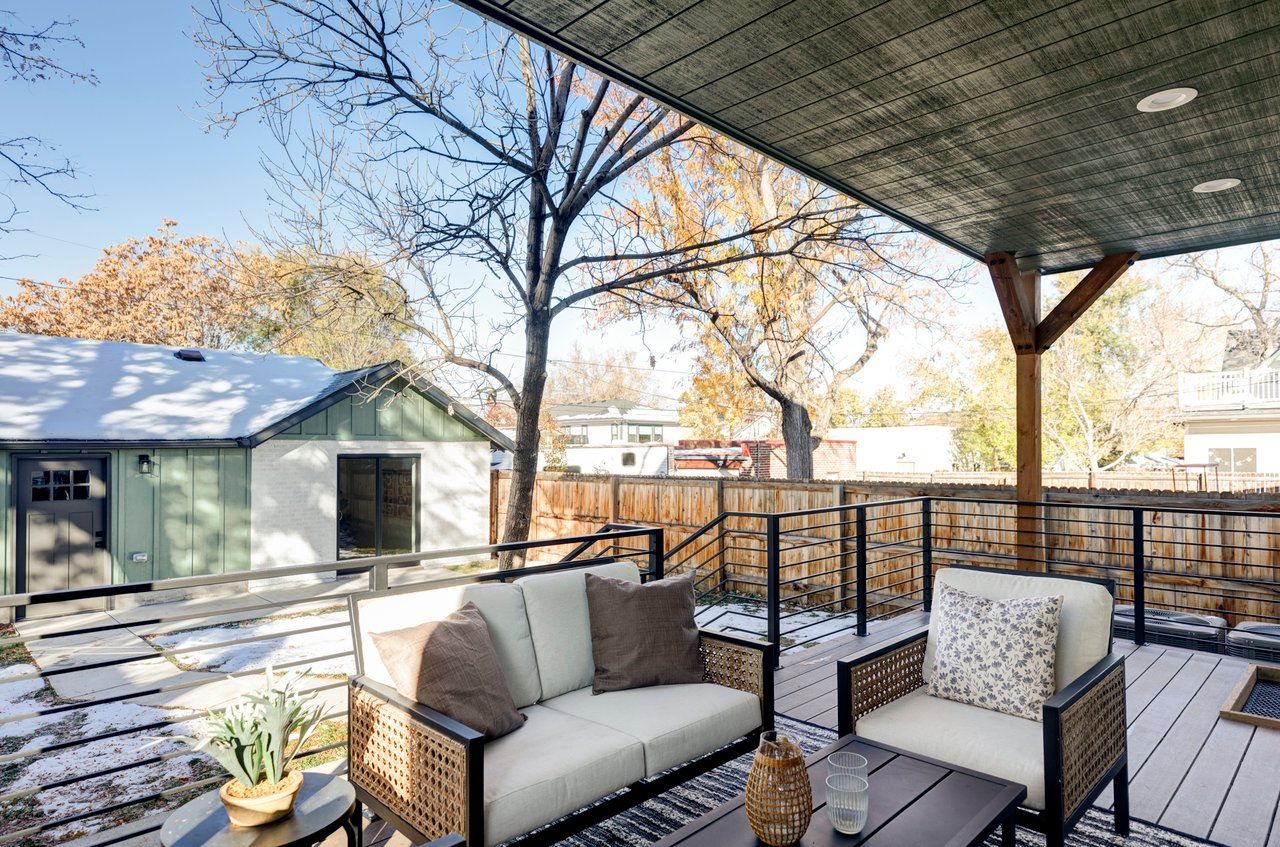 Covered backyard patio with lounge area with two couches and a coffee table, overlooking garage and ADU