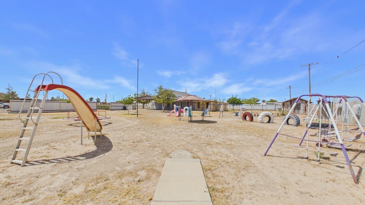 Outdoor playground with a large slide, swings, and climbing equipment on dry ground.