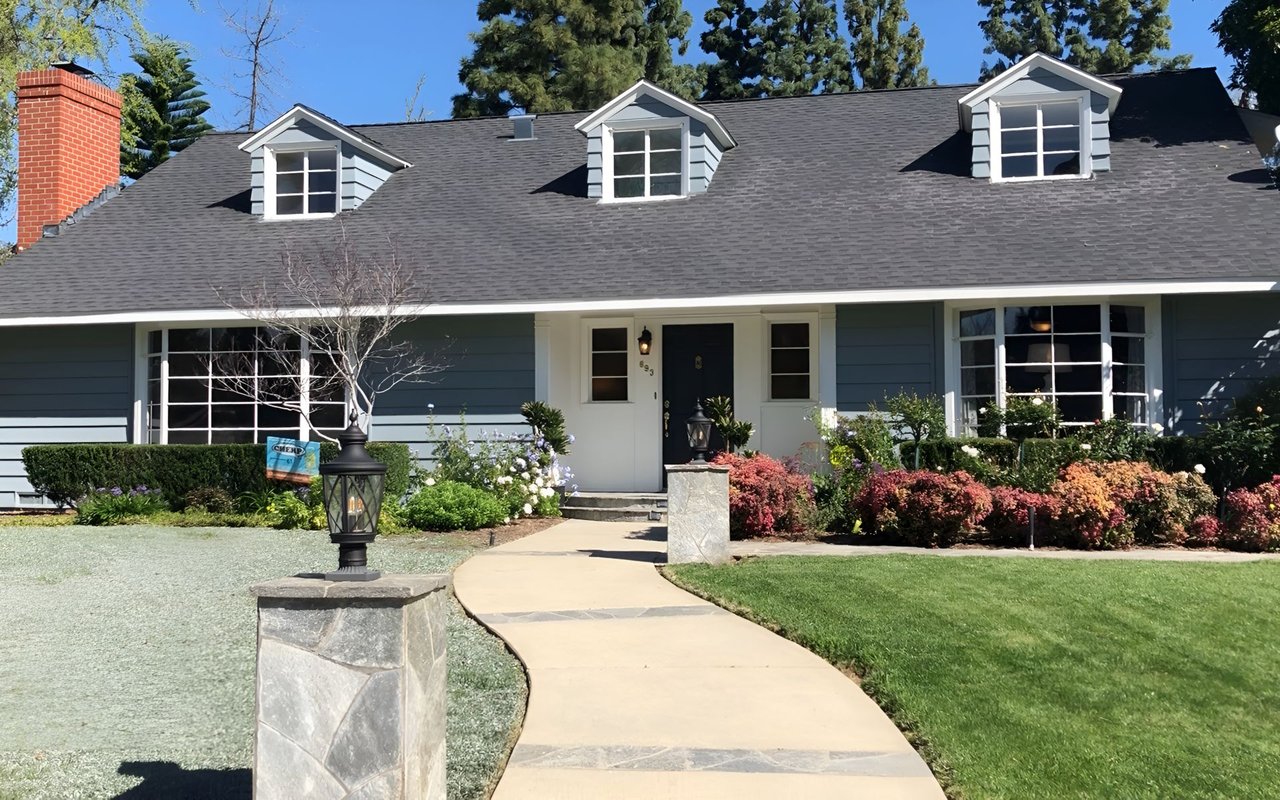Blue-gray house with three dormers, a brick chimney, and a curved front walkway.