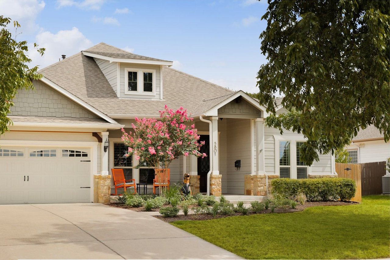 House exterior with a two-car garage, covered porch, and pink flowering tree.